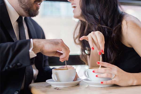 a smiling couple stirring their coffee as they laugh